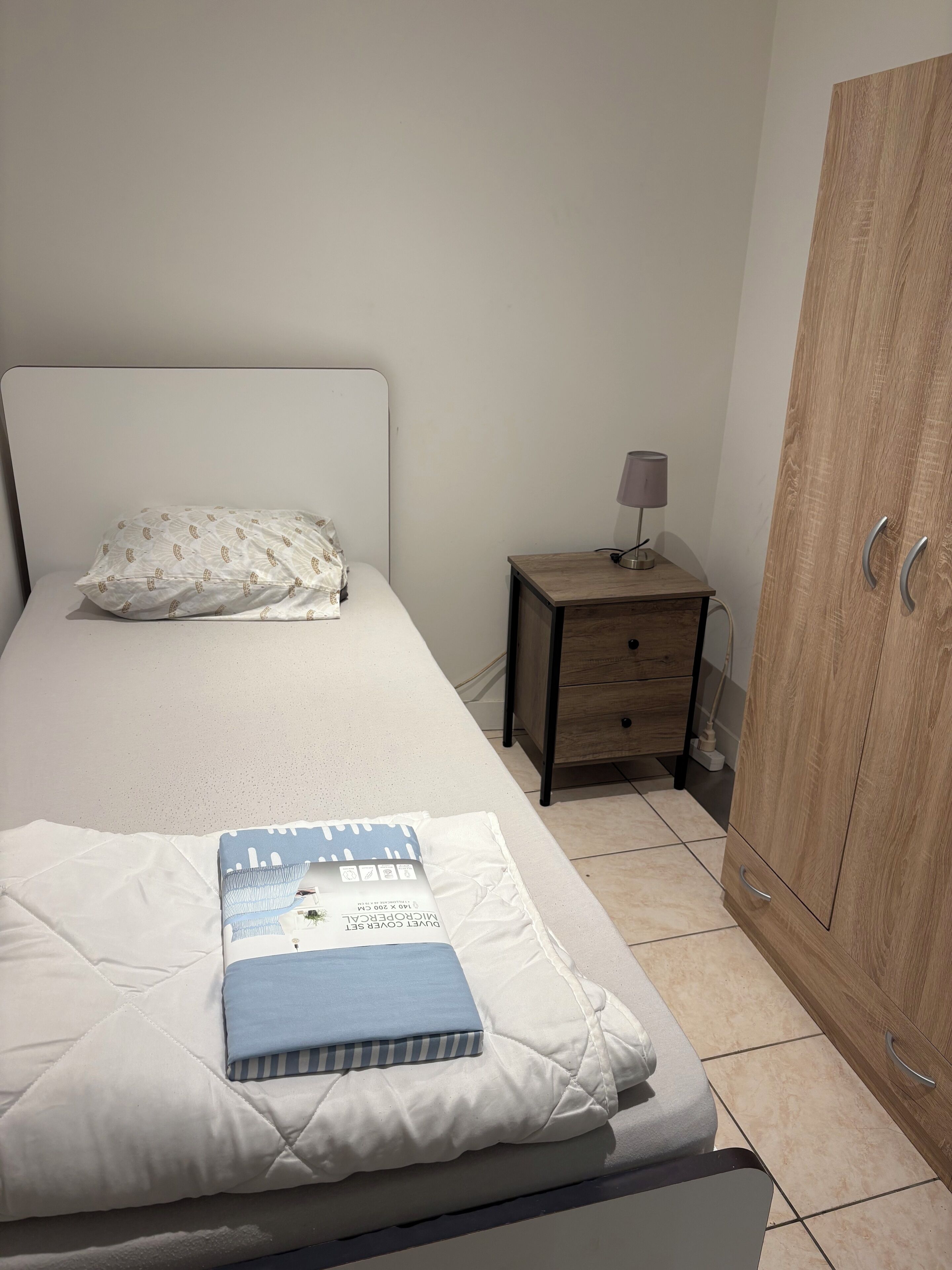 Un lit bien fait, avec un oreiller, une table de chevet avec une lampe et une armoire en bois.