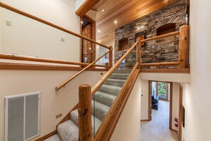 A staircase with wooden railings, a stone wall, and a view of the interior. - Vista Pines Lakeview by Tahoe Getaways - Luxury 4BR w Forested Yard & Short Drive to Lake! (Tahoe Vista)