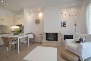 Ein modernes Wohnzimmer mit Kamin, weißen Möbeln und einer Küche im Hintergrund.