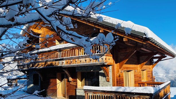 Eine Holzhütte mit Balkon, auf Stein gegründet, umgeben von Schnee.