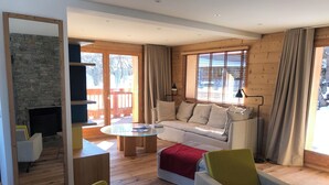 Ein modernes Wohnzimmer mit Kamin aus Stein, Holzboden, einer großen Couch und einem Glastisch.