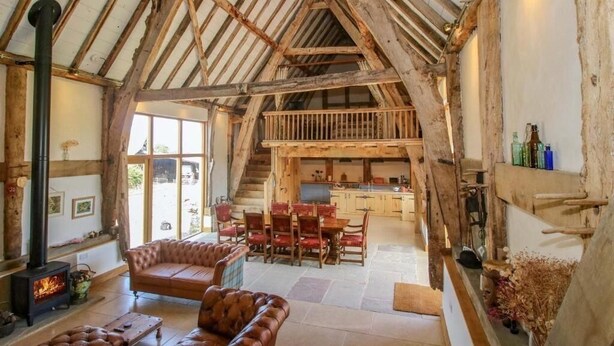 Een rustiek interieur met zichtbare houten balken, een open haard, leren banken en een eethoek.