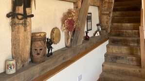 Een rustiek interieur met zichtbare houten balken, een houten trap en diverse decoratieve objecten op een plank.