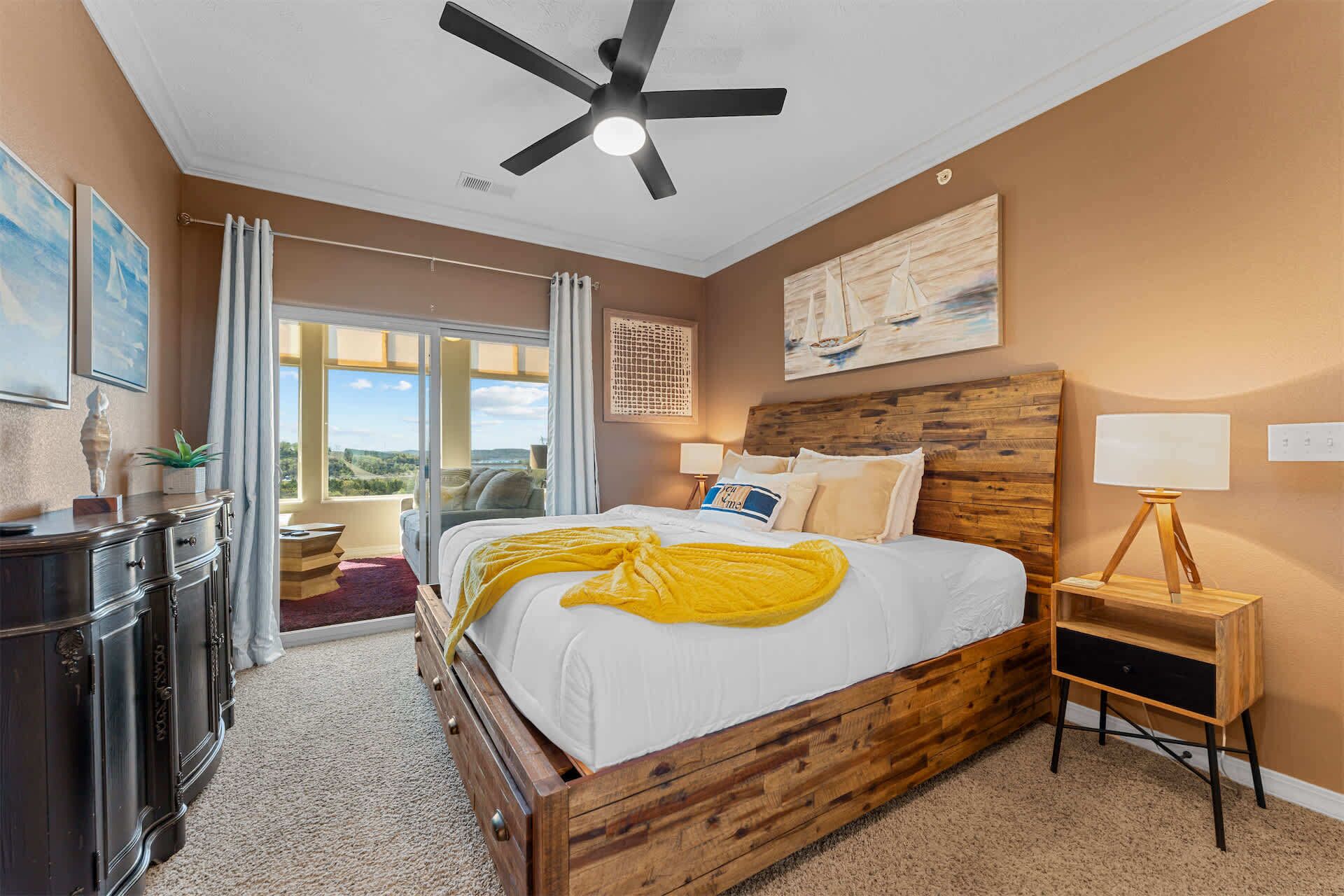 A bedroom with a bed, a ceiling fan, a nightstand, a lamp, and a view through the window.