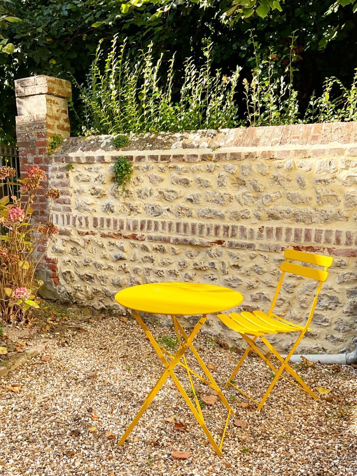 A yellow table and chair set against a stone wall with a brick chimney.