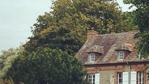 Un bâtiment historique à la façade en pierre, doté de nombreuses fenêtres et surmonté d’un grand arbre en arrière-plan.