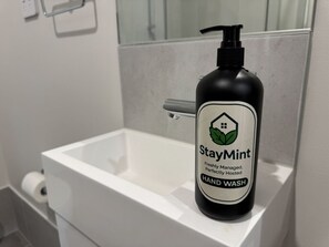 Eine schwarze Flasche StayMint Handseife auf einem weißen Waschtisch.