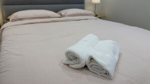 Un lit bien fait, avec une tête de lit grise, deux oreillers et une serviette blanche pliée posée sur le lit.