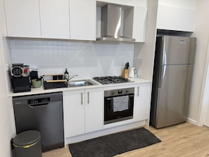 Eine moderne Küche mit weißen Schränken, einem Edelstahlkühlschrank, einem eingebauten Backofen und einem Geschirrspüler.