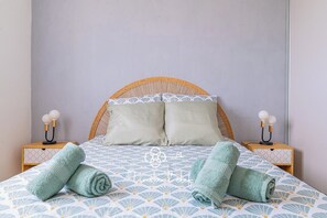 Ein Bett mit einem gewobenen Kopfteil, zwei Nachttische mit Lampen und zusammengerollten Handtüchern auf dem Bett.
