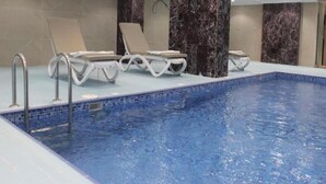 Une piscine avec des chaises longues et une colonne en marbre.