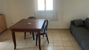 Zona pranzo con tavolo e sedie in legno, finestra con tende, divano e mobiletto in legno.