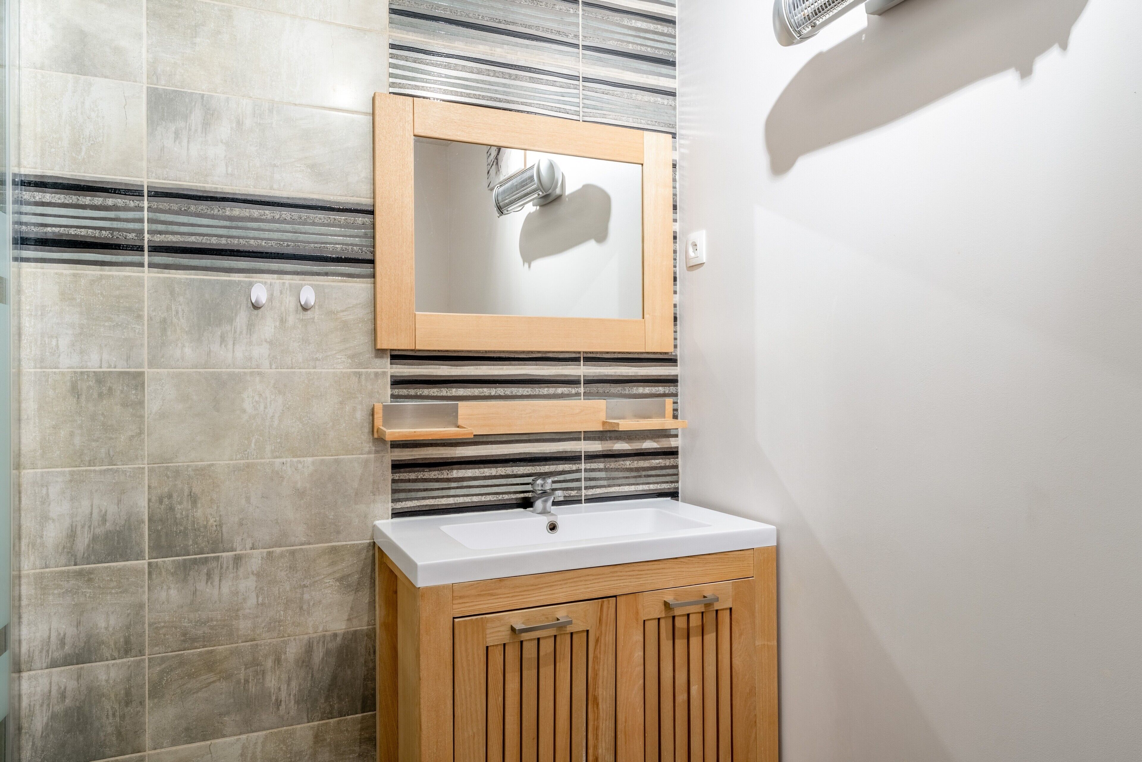 Ein Badezimmer mit einem weißen Waschbecken, Holzschränken und einem Spiegel mit Holzrahmen.