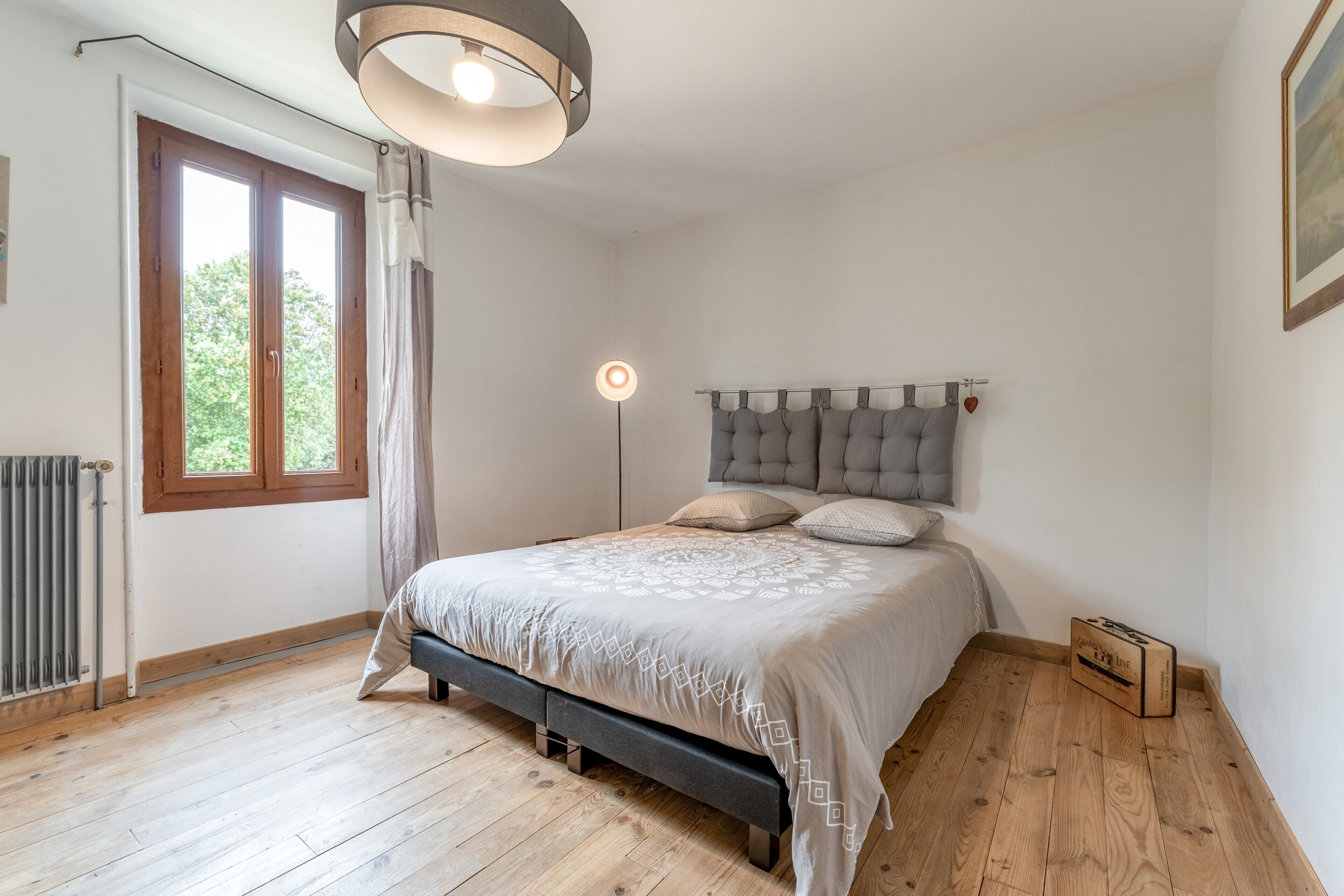 A bedroom with a bed, a radiator, a window, a floor lamp, and a framed picture on the wall.