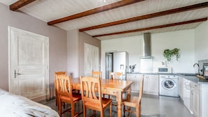 Een kamer met een bed, een houten eettafel, stoelen, een wasmachine en een keuken met kastjes en een magnetron.