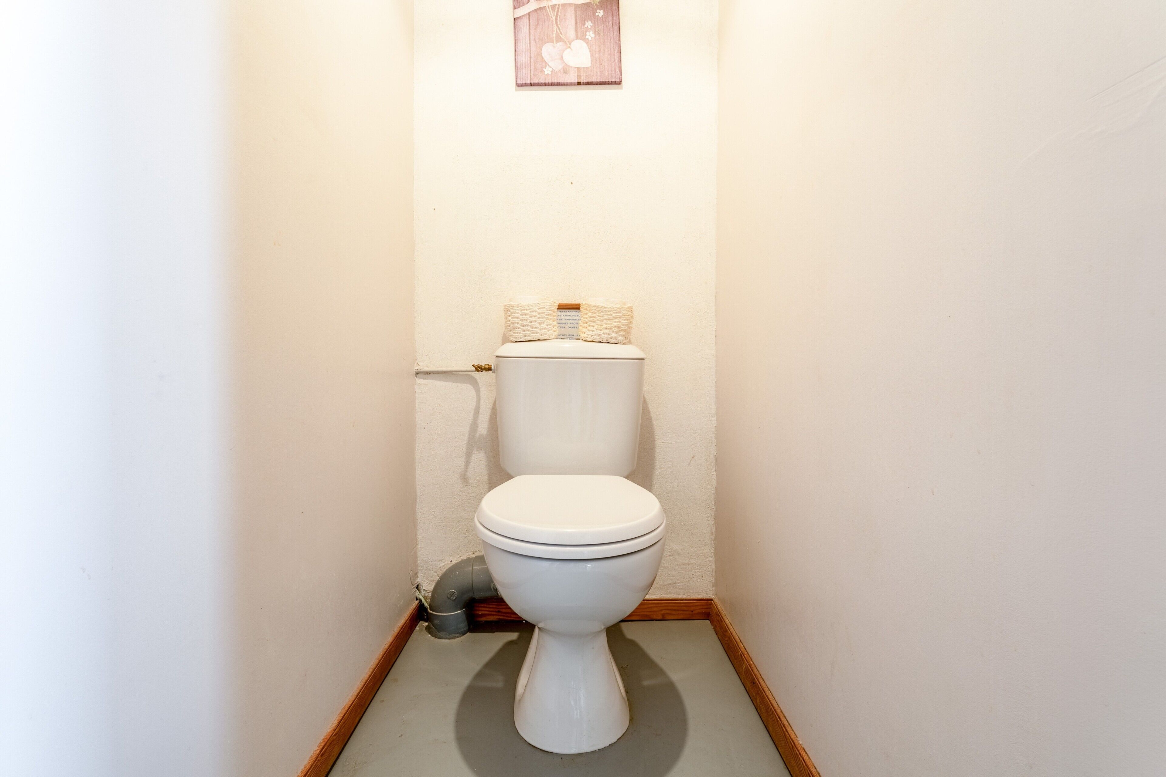 Un baño pequeño y estrecho, con un inodoro blanco, suelo de madera y una repisa sobre el inodoro.