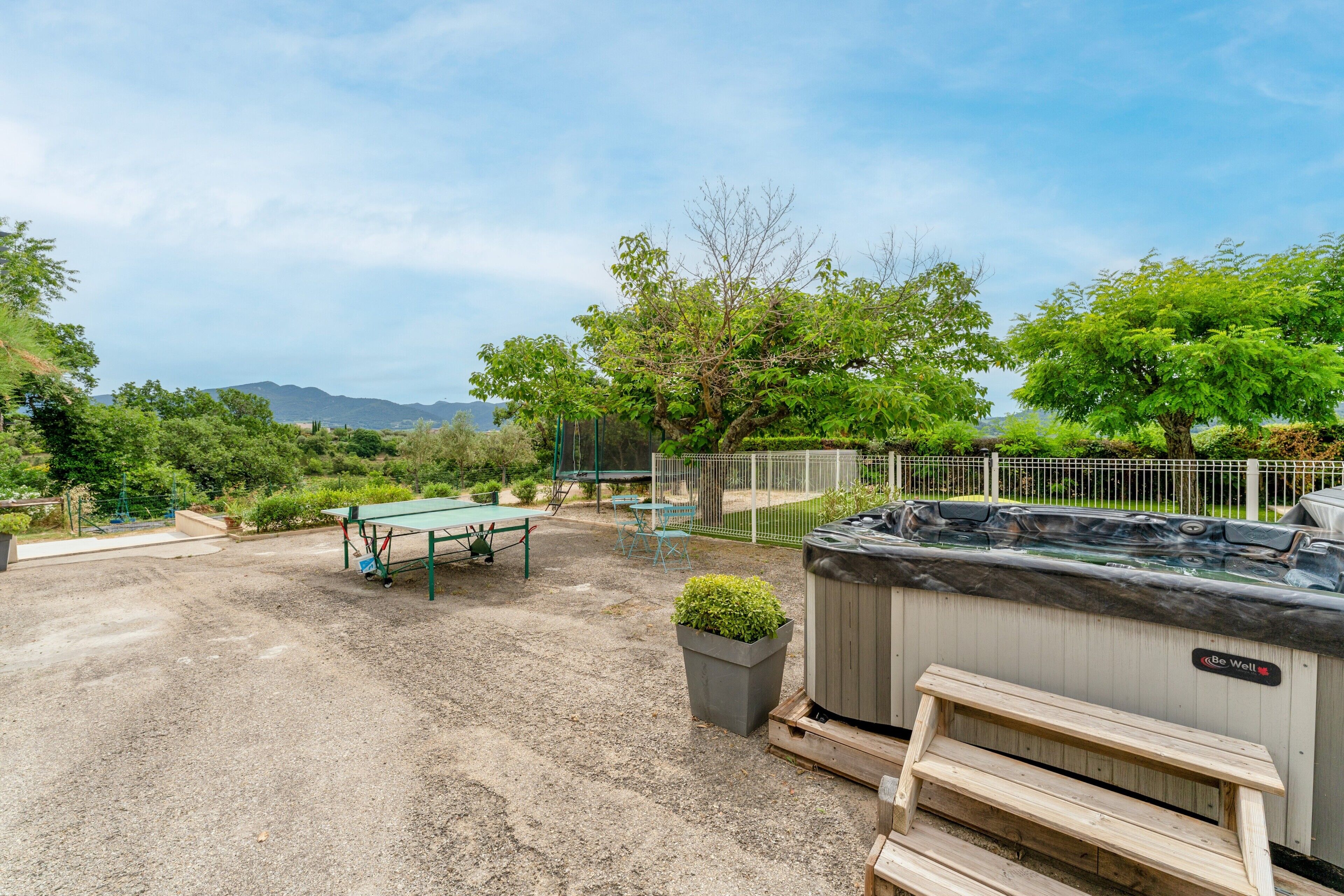 Un bain à remous, une terrasse en bois et un espace extérieur aménagé avec des sièges, offrant une vue sur les arbres et les montagnes.