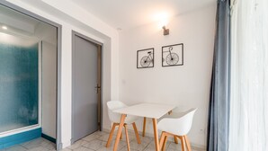 Ein Zimmer mit einem weißen Tisch, Stühlen, einer Tür und zwei gerahmten Bildern an der Wand.