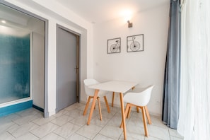 A room with a white table and chairs, a door, and two framed pictures on the wall. - Gite Lavande – La Bastide St Jacques (Vinsobres)