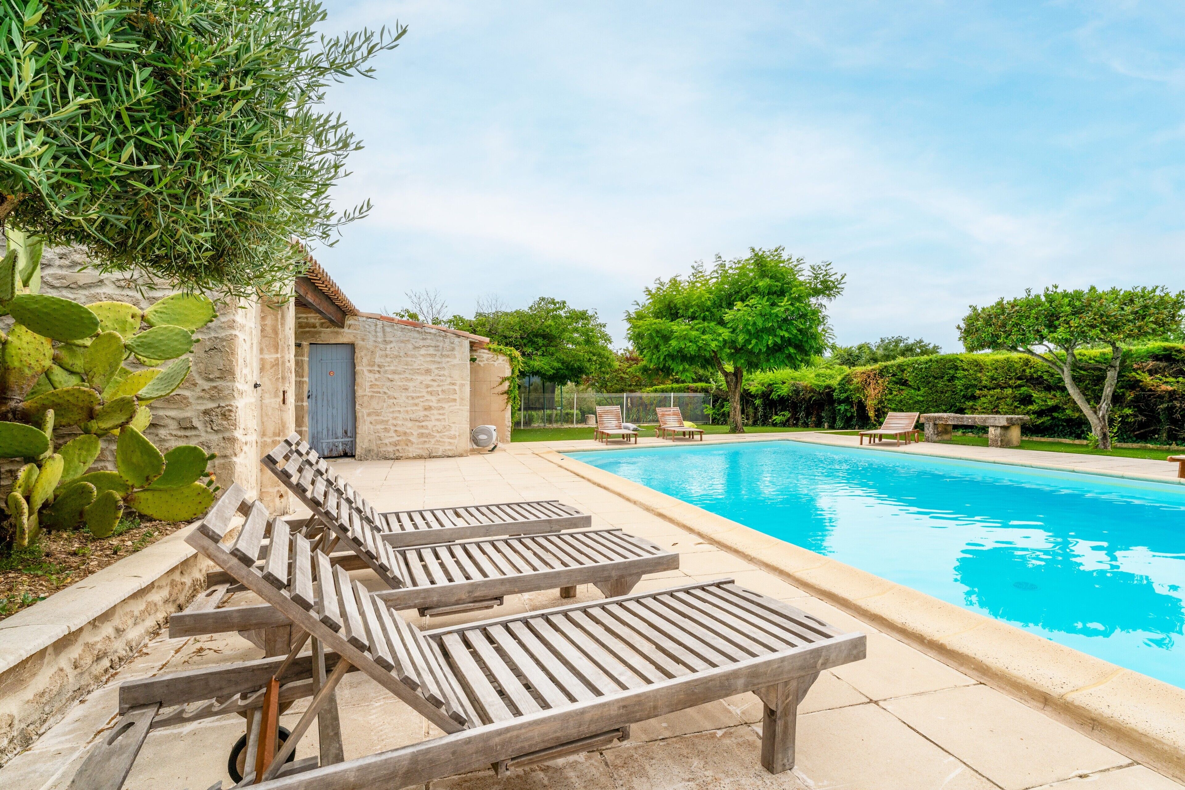Une piscine entourée de chaises longues, un bâtiment en pierre et de la verdure.