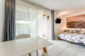 A bedroom with a bed, a TV mounted on the wall, and a large window with curtains. - Gite Lavande – La Bastide St Jacques (Vinsobres)