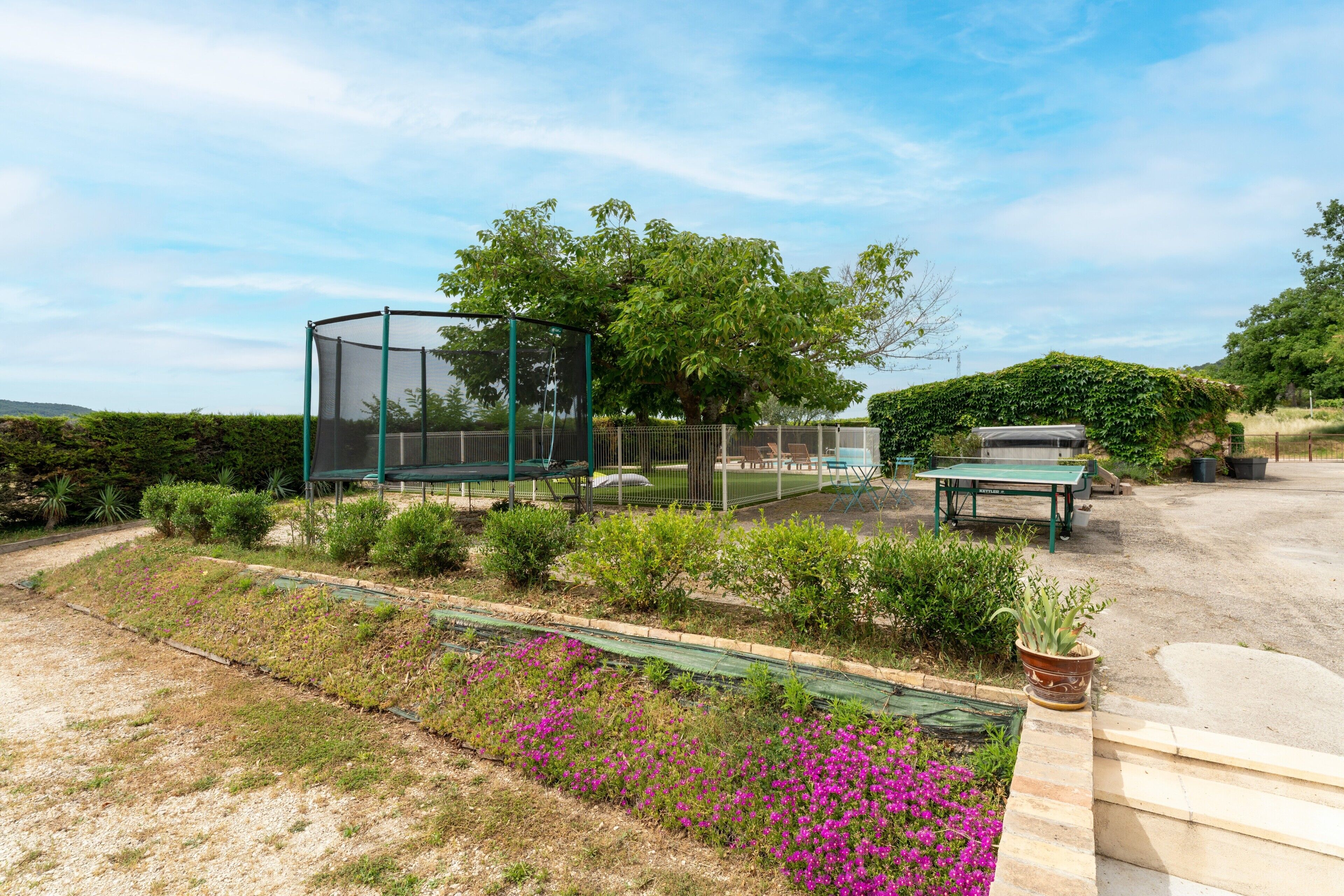 Um jardim com um banco verde, uma mesa e uma estrutura de pérgola.