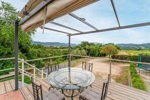 A glass-top table with four chairs on a wooden deck, overlooking a vineyard and hills. - Gite les vignes – La Bastide St Jacques: Provençal Retreat Amidst Organic Vineyards (Vinsobres)