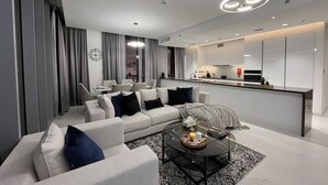 A modern living room with a sofa, coffee table, and a kitchen area in the background. - Maison Privee - Modern Family Retreat w/ Dubai Skyline Views (Dubai)