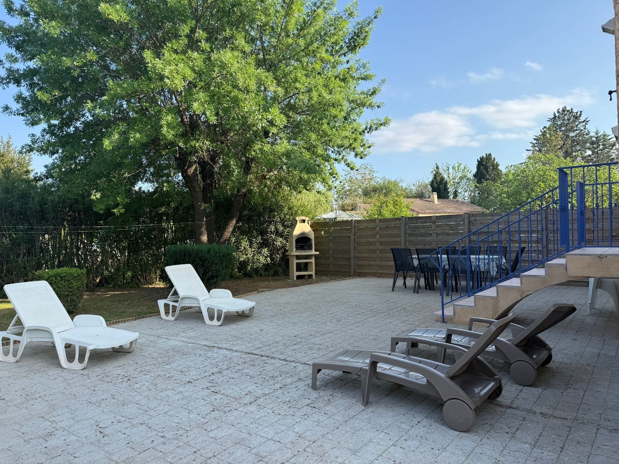 Ein Außenbereich mit einer Terrasse, Lounge-Möbeln, einem Grill und einer blauen Treppe.