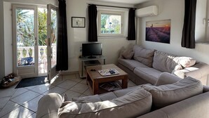 En stue med sofa, sofabord, fjernsyn og en skydedør til et udendørs område.