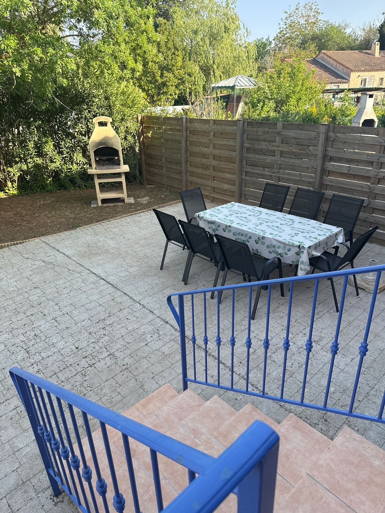 A patio with a table and chairs, a barbecue grill, and a wooden fence.