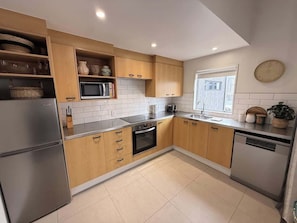 Una cocina moderna con armarios de madera, un refrigerador de acero inoxidable, un horno, un lavavajillas y un ventanal con vistas.