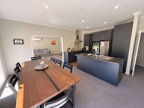 Una cocina moderna con armarios grises, una isla central y una zona de comedor con mesa y sillas de madera.