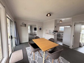 Ett kompakt bostadsutrymme med en matplats, ett litet kök och en skjutdörr som leder ut till ett utomhusområde.