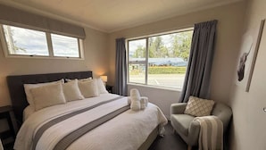 Una habitación de hotel con una cama grande, una silla, un ventanal y una puerta.