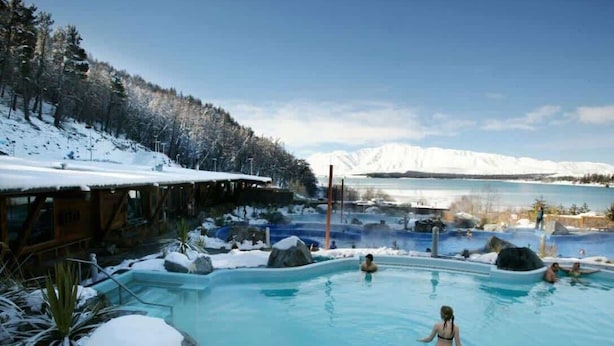 Zona de piscina con alrededores nevados y una montaña al fondo.