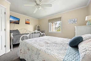 A bedroom with a bed, a ceiling fan, a TV, a window, and a wall with a picture and a sign. - Charming 1 Bedroom, Two Bath Condo in Desirable North Ocean City (Ocean City)