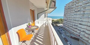 Un balcon avec une table et des chaises, donnant sur une rue et un immeuble de grande hauteur.