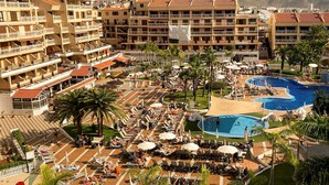 Ett semesterhotell med flera pooler, solstolar och utsikt över de omgivande byggnaderna.