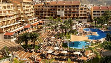 A resort with multiple swimming pools, sun loungers, and a view of the surrounding buildings.