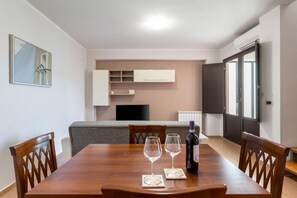 Ein Essbereich mit einem Holztisch, zwei Weingläsern und einer Weinflasche. Im Hintergrund befinden sich eine graue Couch und eine weiße Kommode.