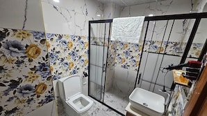 Een badkamer met toilet, bidet en wastafel, marmeren wanden en een douchegedeelte.