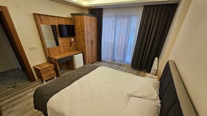 Een hotelkamer met een bed, een houten bureau, een televisietoestel en een groot raam met gordijnen.