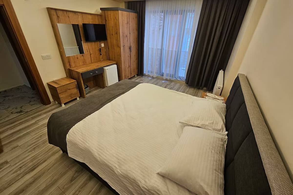 Una habitación de hotel con cama, un escritorio de madera, televisor y un ventanal con cortinas.