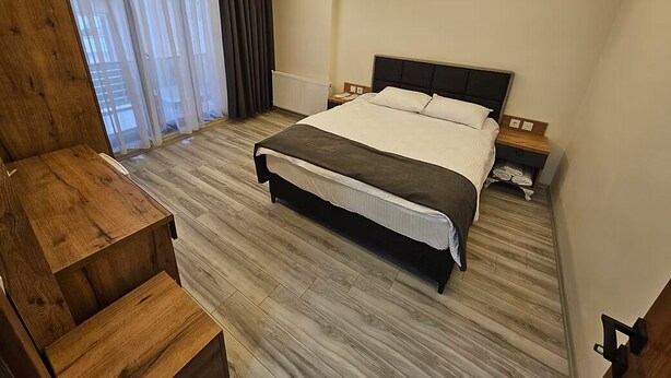 Een moderne hotelkamer met een groot bed, houten meubels en uitzicht door dunne gordijnen.