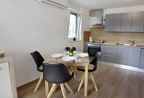A modern kitchen with grey cabinets, a built-in oven, and a dining area with a glass table and black chairs. - Comfort Apartment in Zambratija (Umag)