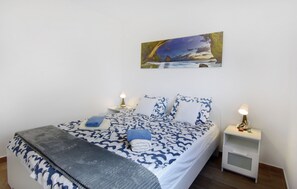 A neatly made bed with a patterned bedspread, two bedside tables with lamps, and a painting above the bed. - Comfort Apartment in Zambratija (Umag)