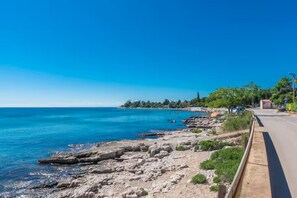 A coastal road with rocky terrain, a clear blue sky, and a distant shoreline. - Comfort Apartment in Zambratija (Umag)