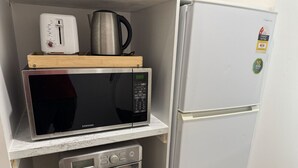 Una kitchenette compacta con microondas, tostadora y cafetera en un estante, un refrigerador y un horno.