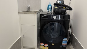 Un área de lavandería compacta con lavadora, plancha y lavabo.